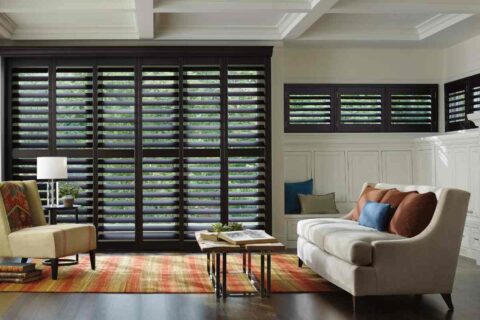 Brown Hunter Douglas plantation shutters blocking light in a traditional living room near Richmond, VA.